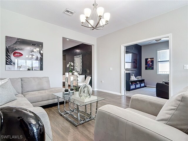 living room featuring a chandelier, visible vents, baseboards, and wood finished floors