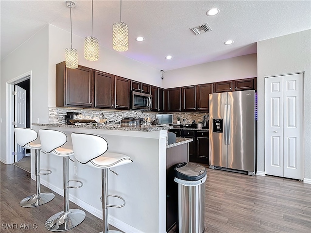 kitchen featuring a breakfast bar area, visible vents, appliances with stainless steel finishes, dark brown cabinets, and a peninsula