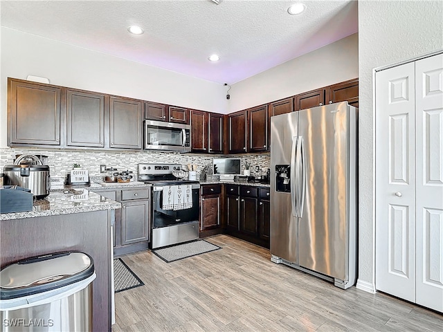 kitchen with dark brown cabinetry, light wood-style flooring, stainless steel appliances, and backsplash