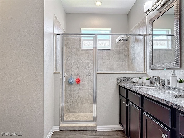 full bathroom featuring double vanity, a textured wall, a sink, a shower stall, and wood finished floors