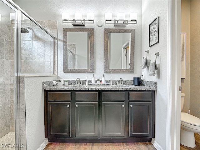 full bathroom featuring double vanity, toilet, a stall shower, a sink, and wood finished floors