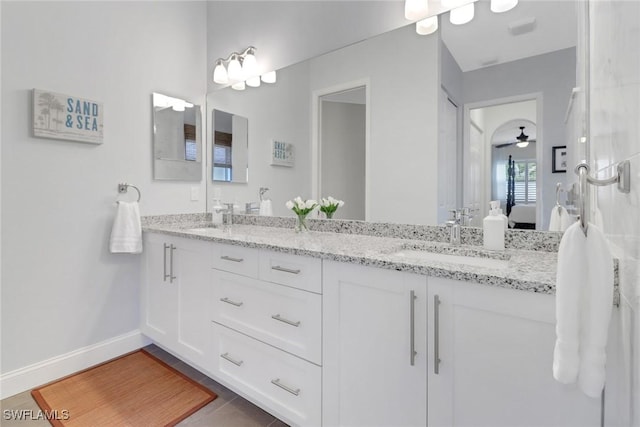 ensuite bathroom featuring baseboards, double vanity, a sink, and connected bathroom