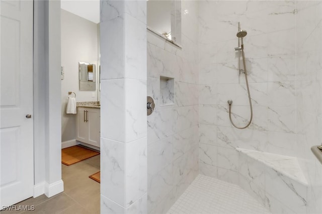 full bath featuring tiled shower, vanity, and baseboards