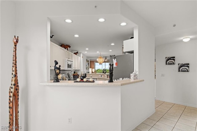 kitchen with white microwave, a peninsula, white cabinets, light countertops, and freestanding refrigerator