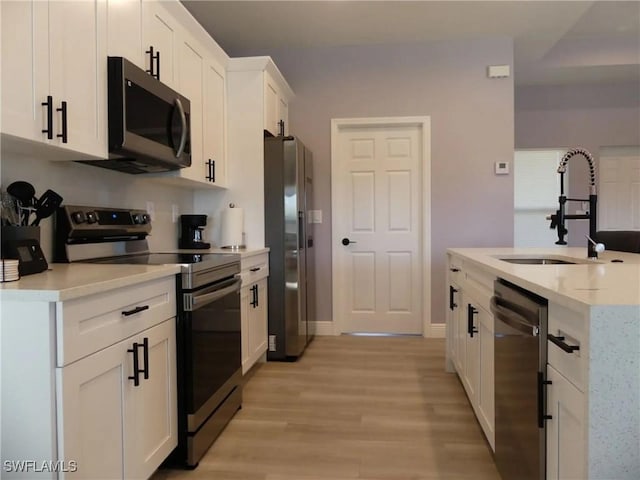 kitchen featuring stainless steel appliances, a sink, white cabinets, light countertops, and light wood-type flooring