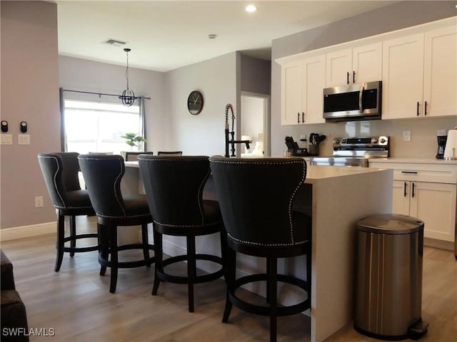 kitchen featuring a kitchen island with sink, appliances with stainless steel finishes, white cabinets, and light countertops