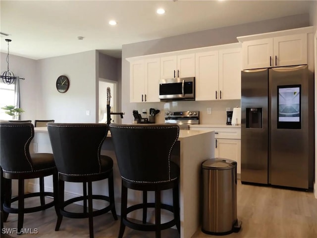 kitchen with stainless steel appliances, decorative light fixtures, a kitchen island with sink, and white cabinets