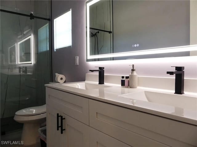 bathroom with toilet, double vanity, a sink, and a marble finish shower