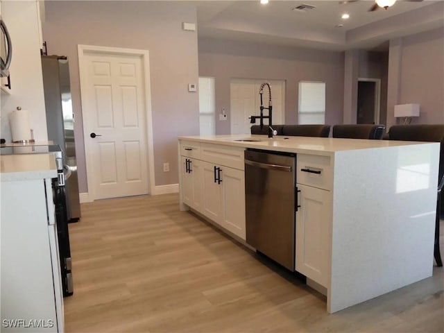 kitchen featuring a sink, white cabinets, open floor plan, light countertops, and stainless steel dishwasher