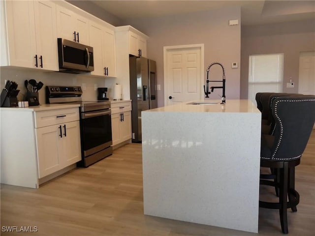 kitchen featuring white cabinets, an island with sink, appliances with stainless steel finishes, light countertops, and a sink