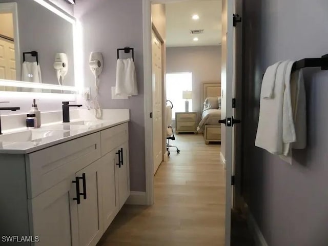 ensuite bathroom featuring connected bathroom, a sink, wood finished floors, visible vents, and double vanity