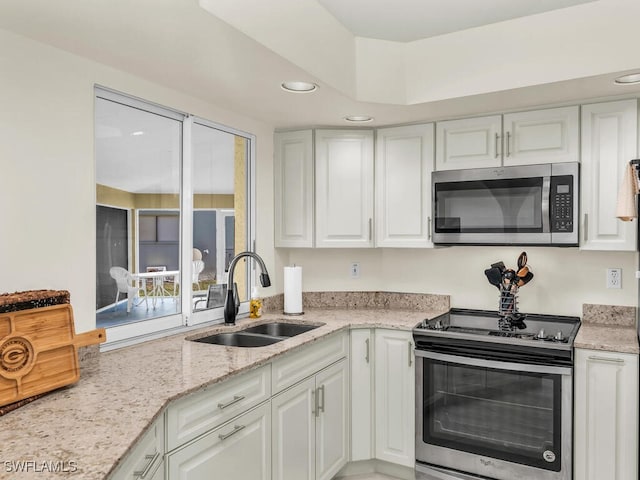 kitchen with stainless steel appliances, white cabinets, a sink, and light stone countertops