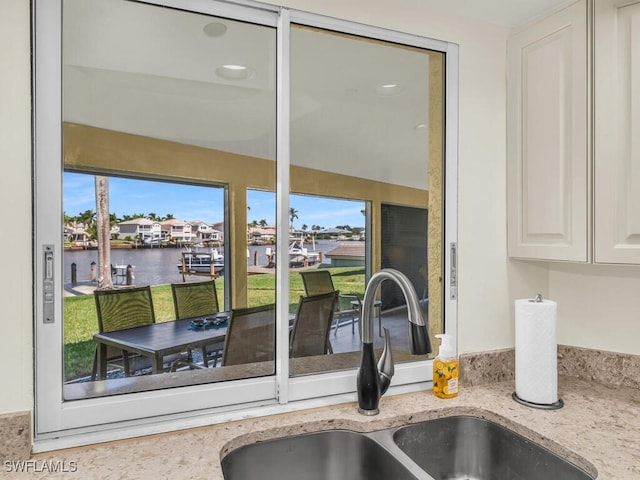 interior space with a water view, light stone countertops, white cabinets, and a sink