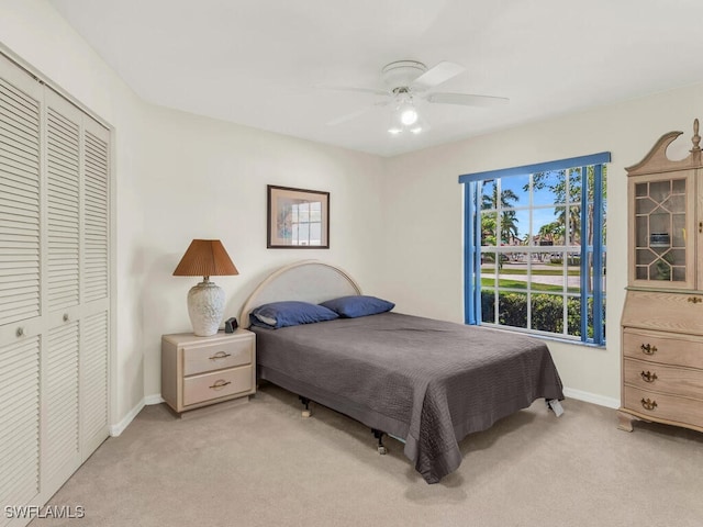 bedroom featuring baseboards, ceiling fan, a closet, and light colored carpet