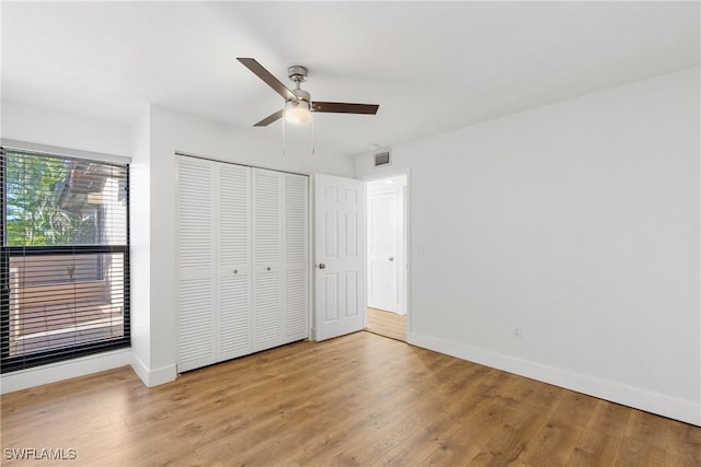 unfurnished bedroom featuring baseboards, visible vents, ceiling fan, wood finished floors, and a closet