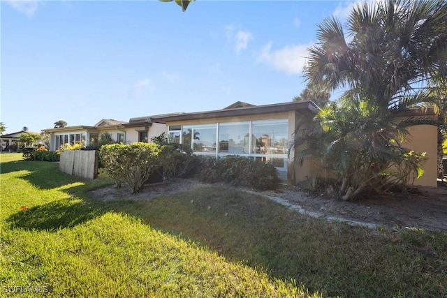 rear view of property featuring a sunroom, a yard, and stucco siding