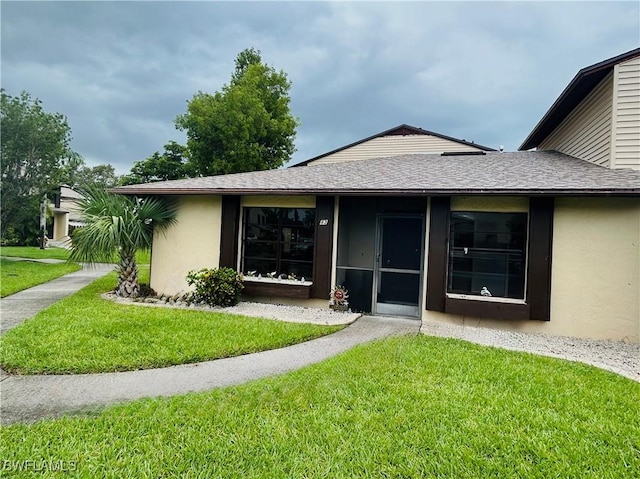 back of property featuring a shingled roof, a lawn, and stucco siding