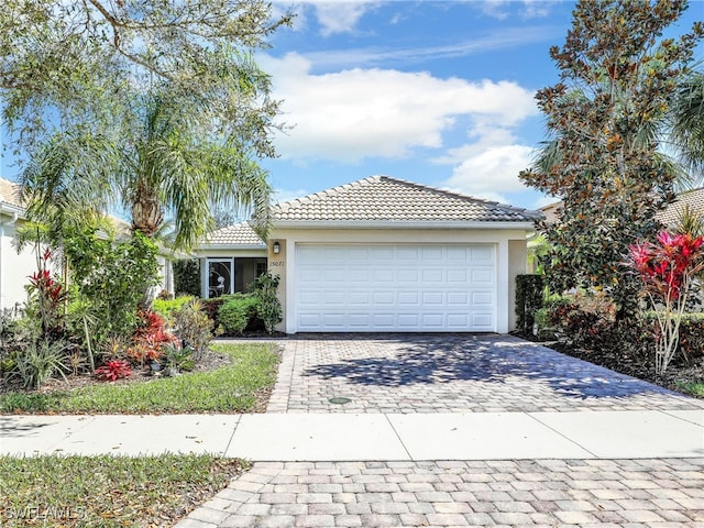 ranch-style home featuring decorative driveway, an attached garage, a tile roof, and stucco siding