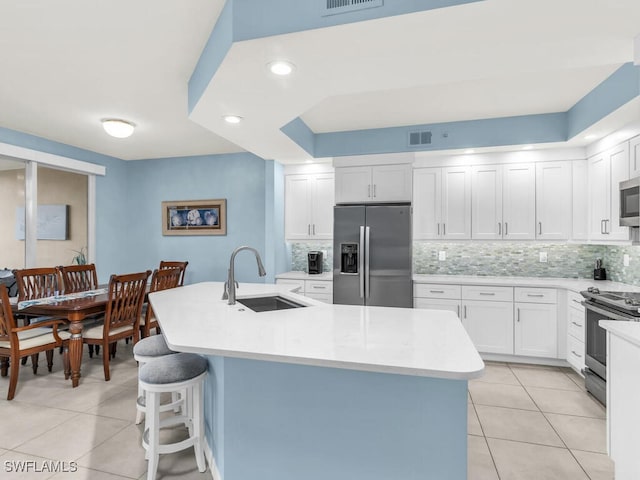 kitchen with a kitchen island with sink, stainless steel appliances, a sink, and light countertops