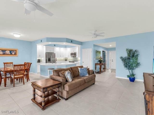 living area featuring light tile patterned floors, a ceiling fan, and baseboards