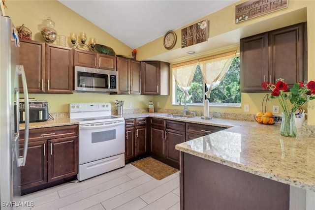 kitchen featuring light stone counters, a peninsula, vaulted ceiling, stainless steel appliances, and a sink