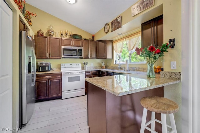 kitchen featuring appliances with stainless steel finishes, vaulted ceiling, a sink, a peninsula, and a kitchen breakfast bar