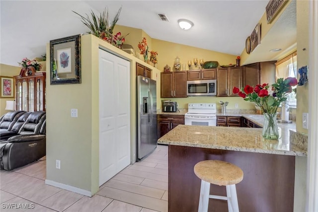 kitchen with light stone counters, a breakfast bar area, appliances with stainless steel finishes, vaulted ceiling, and a peninsula