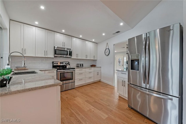 kitchen featuring stainless steel appliances, a sink, white cabinetry, light stone countertops, and light wood finished floors