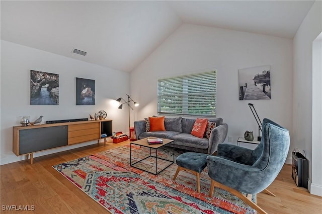 living area featuring light wood finished floors, visible vents, and high vaulted ceiling