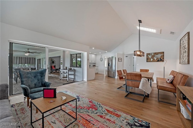 living area featuring light wood finished floors, visible vents, and high vaulted ceiling