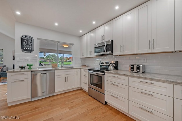 kitchen with a sink, white cabinetry, light wood-style floors, appliances with stainless steel finishes, and decorative backsplash