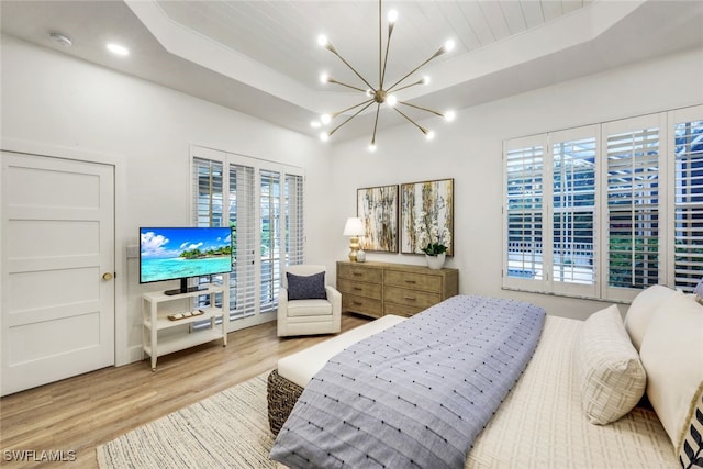 bedroom with access to outside, a raised ceiling, a notable chandelier, and wood finished floors