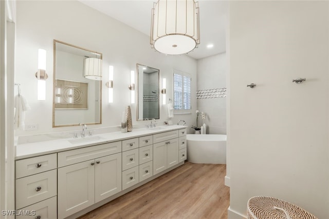 full bathroom featuring a freestanding bath, double vanity, wood finished floors, and a sink