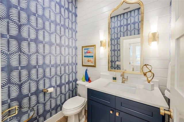 bathroom with toilet, wooden walls, and vanity