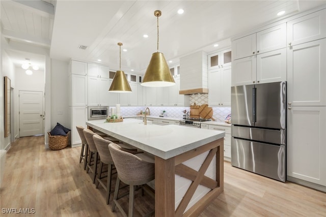 kitchen with decorative light fixtures, stainless steel appliances, custom range hood, glass insert cabinets, and white cabinetry