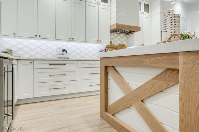 interior space with glass insert cabinets, white cabinetry, backsplash, and light wood finished floors