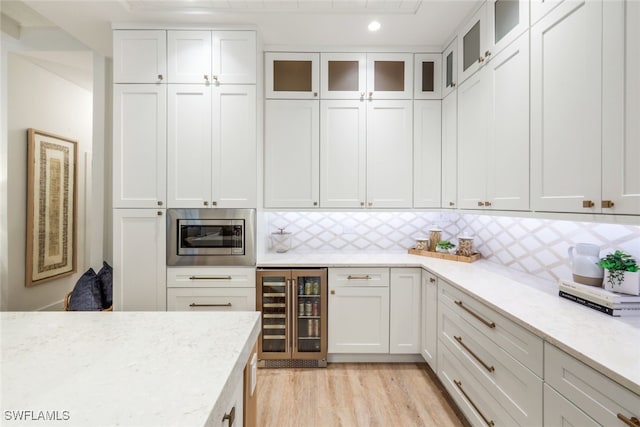 kitchen featuring glass insert cabinets, white cabinetry, wine cooler, and stainless steel microwave