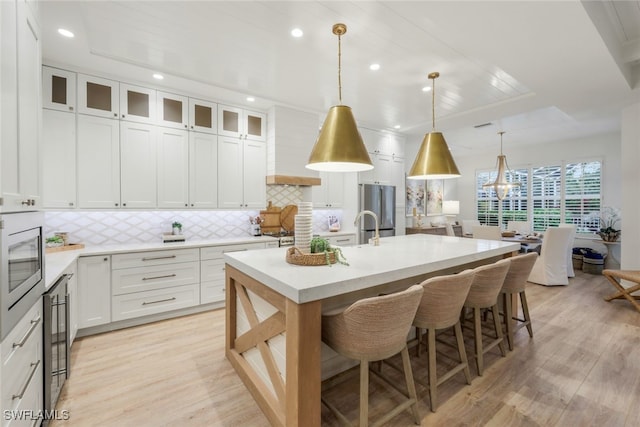 kitchen featuring hanging light fixtures, a kitchen island with sink, white cabinetry, and light countertops