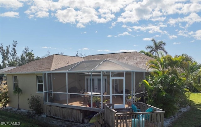 back of house with a shingled roof, glass enclosure, and stucco siding