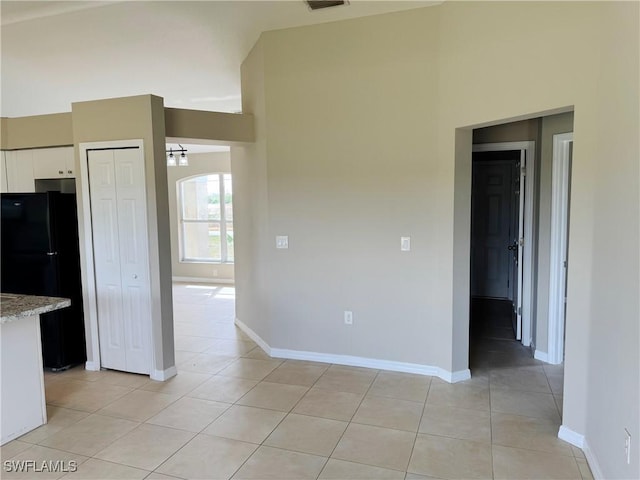 empty room featuring light tile patterned floors, a high ceiling, visible vents, and baseboards