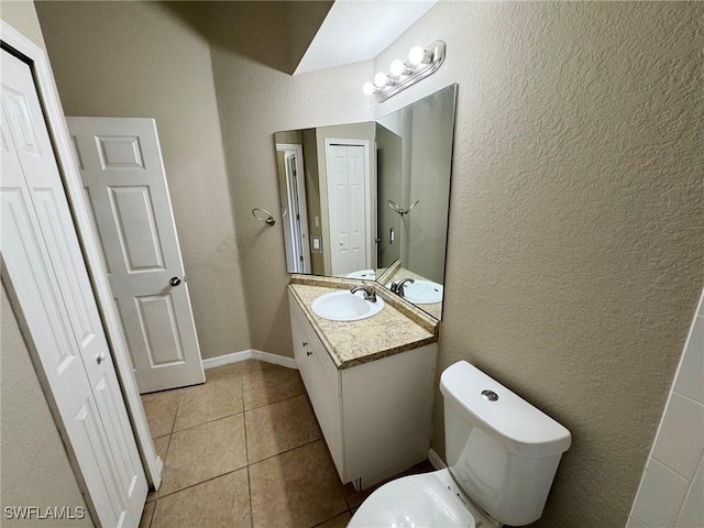 half bathroom with a textured wall, toilet, vanity, baseboards, and tile patterned floors