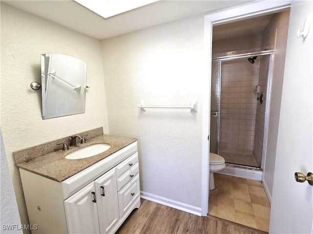 bathroom featuring toilet, a stall shower, vanity, wood finished floors, and baseboards