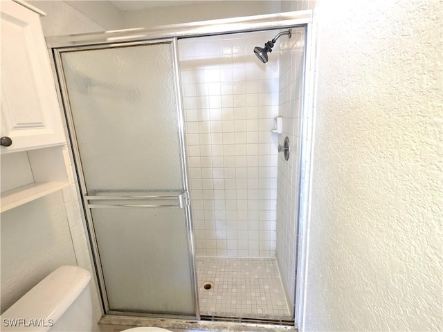 bathroom featuring a textured wall, a stall shower, and toilet