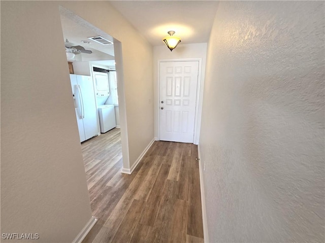 hallway with stacked washer and dryer, baseboards, visible vents, a textured wall, and wood finished floors