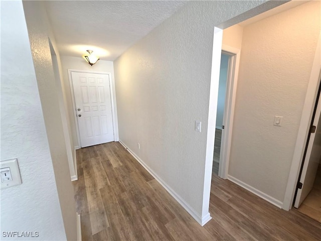 corridor featuring a textured wall, dark wood-style flooring, and baseboards