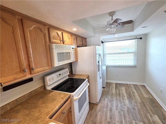 kitchen featuring a tray ceiling, light wood-style flooring, a ceiling fan, white appliances, and baseboards