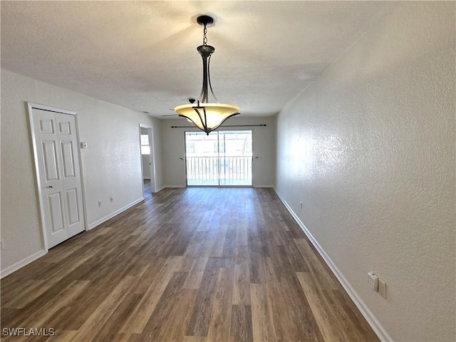 unfurnished dining area with dark wood-style flooring, a textured wall, and baseboards