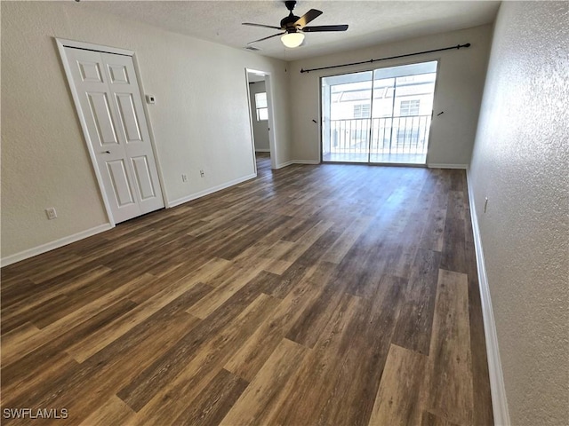 spare room with dark wood-type flooring, a textured wall, baseboards, and a ceiling fan