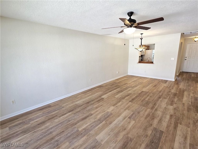 empty room with ceiling fan, a textured ceiling, wood finished floors, visible vents, and baseboards