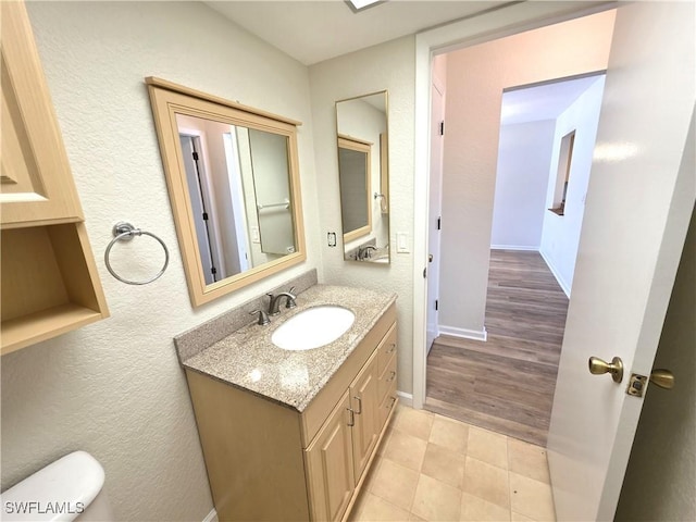 half bathroom with a textured wall, baseboards, and vanity